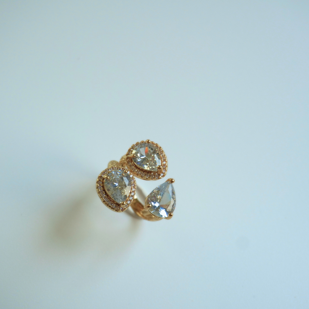 Gold teardrop-shaped earrings with clear gemstones on a light blue background