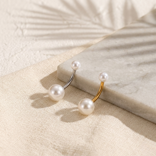 Pair of Pearl belly button rings on a textured surface with a marble block