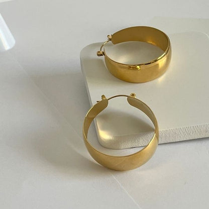 A pair of gold plated wide hoop earrings on a white surface.