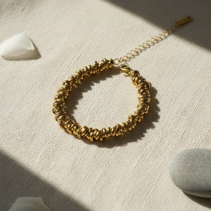 Gold bracelet on a textured beige surface with soft shadows