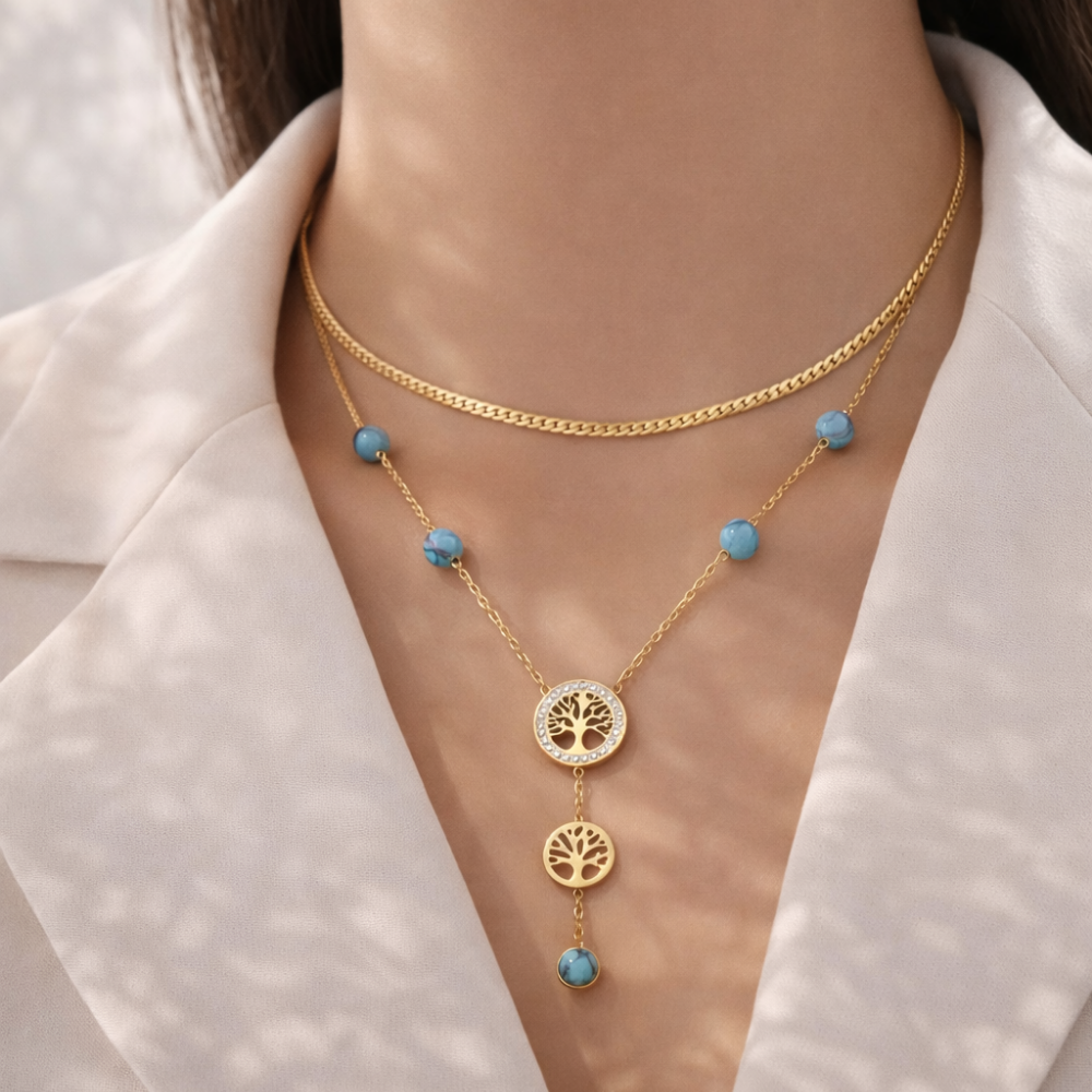 Gold necklace with blue beads and tree-of-life pendants worn by a person in a white outfit.