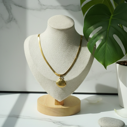 Gold necklace on a mannequin bust with a plant in the background