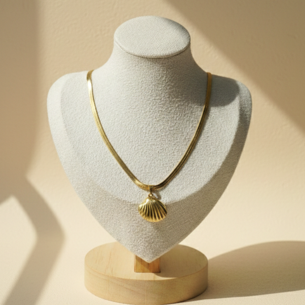 Gold necklace with a shell pendant on a mannequin bust against a beige background