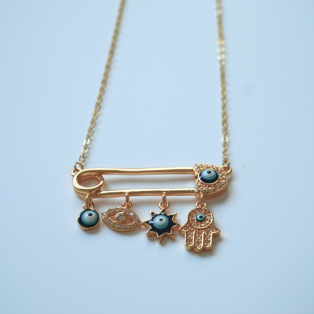 Necklace with gold safety pin and charms on a light blue background