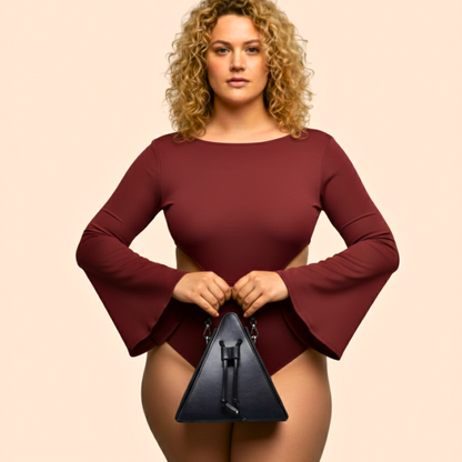 Woman wearing a burgundy long-sleeve top holding a black handbag against a beige background