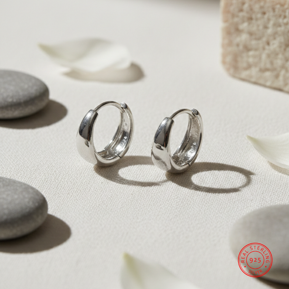 Silver hoop earrings on a light surface with pebbles and leaves
