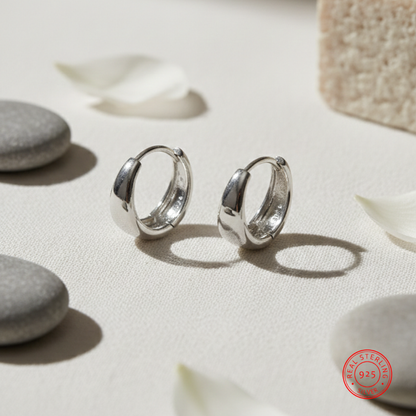 Silver hoop earrings on a light surface with pebbles and leaves