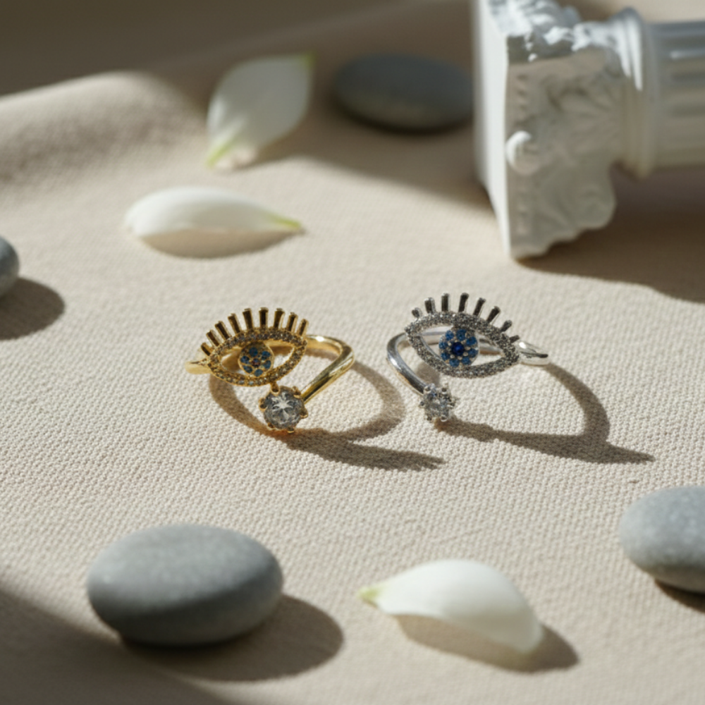 Two decorative rings with gemstones on a textured surface with stones and flowers.