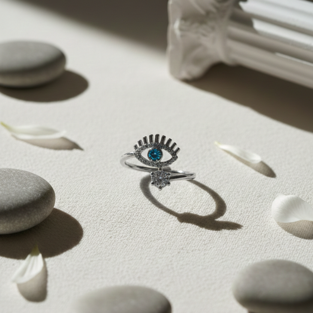 Silver ring with blue gemstone on a light surface with stones and petals