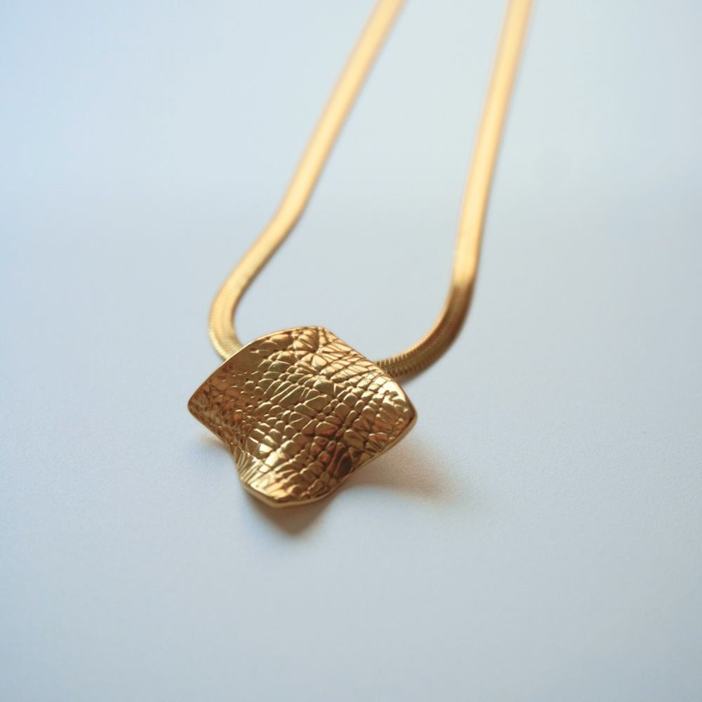 Gold necklace with a textured pendant on a light gray background