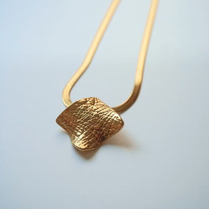 Gold necklace with a textured pendant on a light gray background