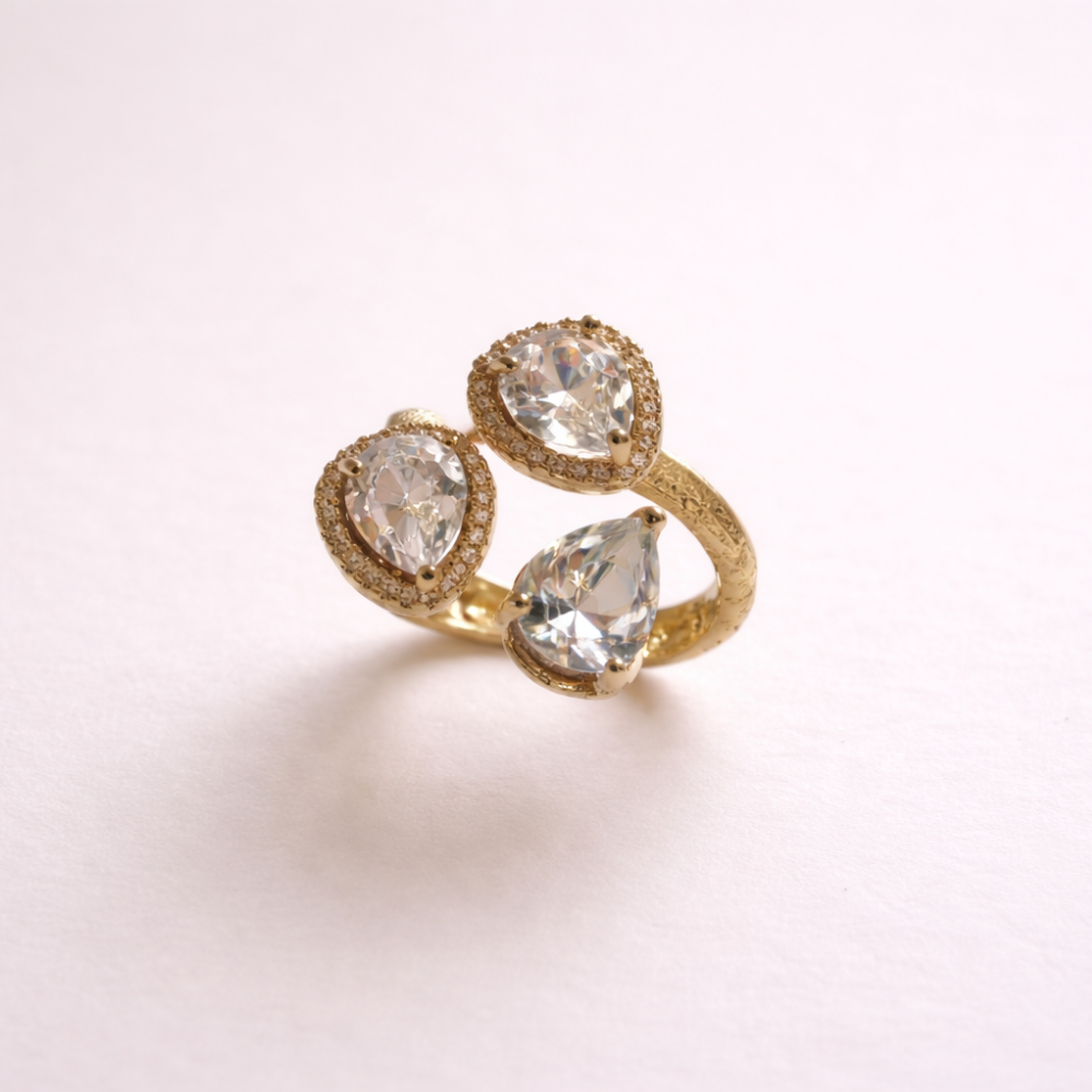 Gold ring with three teardrop-shaped diamonds on a light pink background