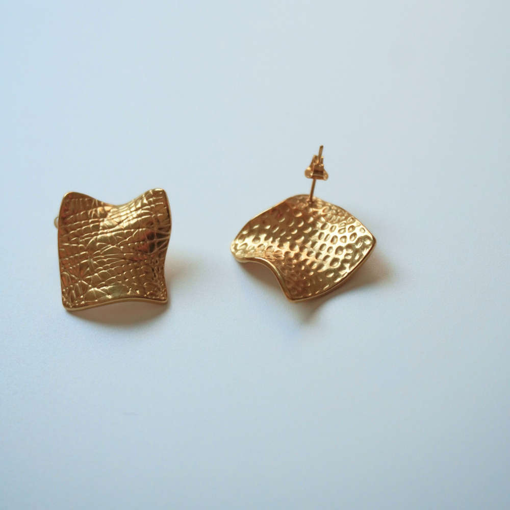 Gold textured earrings on a light blue background