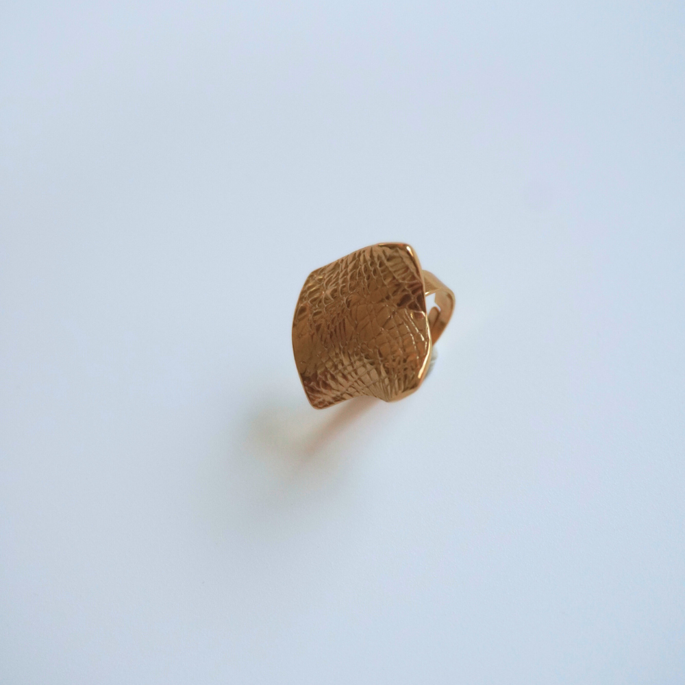 Gold ring with textured design on a light blue background