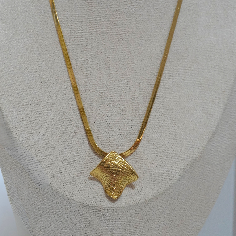 Gold necklace with a textured pendant on a light gray background