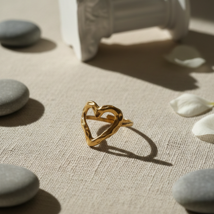 Gold heart-shaped ring on a textured surface with stones and flowers