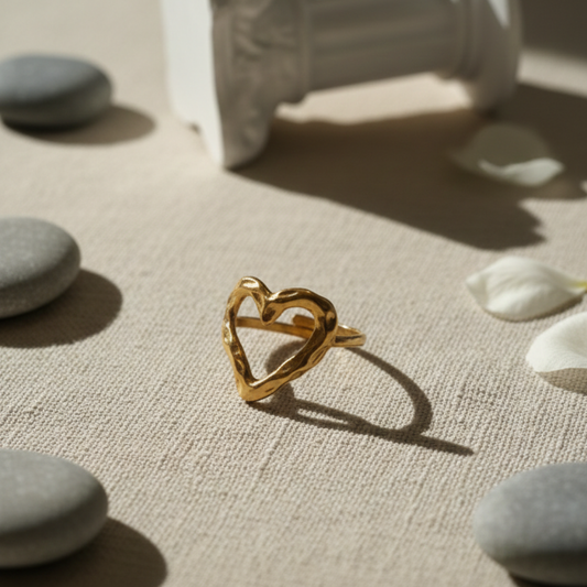 Gold heart-shaped ring on a textured surface with stones and flowers