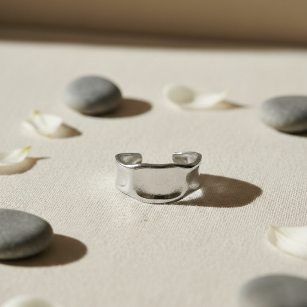 Silver ring on a textured beige surface with stones and small flowers