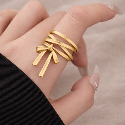 Gold bow-shaped ring on a finger with a blurred background