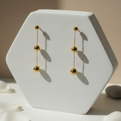 Gold chain earrings on a white hexagonal stand with a neutral background