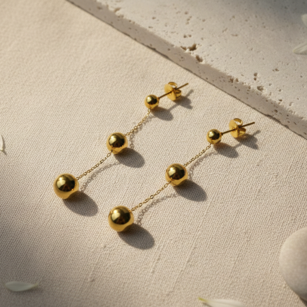 Gold chain earrings on a textured beige surface